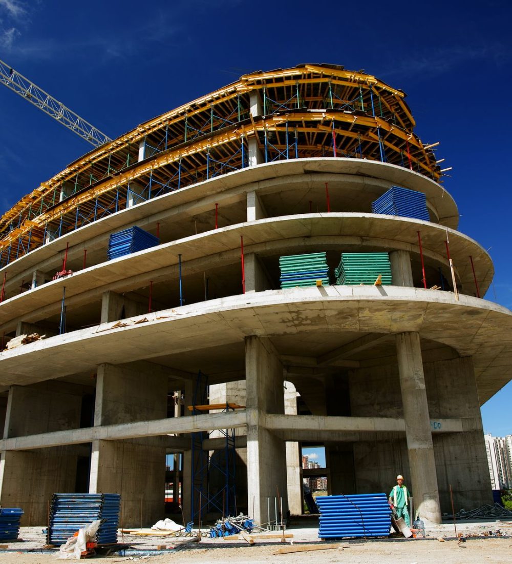 Rohbau eines Gebäudes mit gekrümmter Fassade und Baukran vor blauem Himmel
