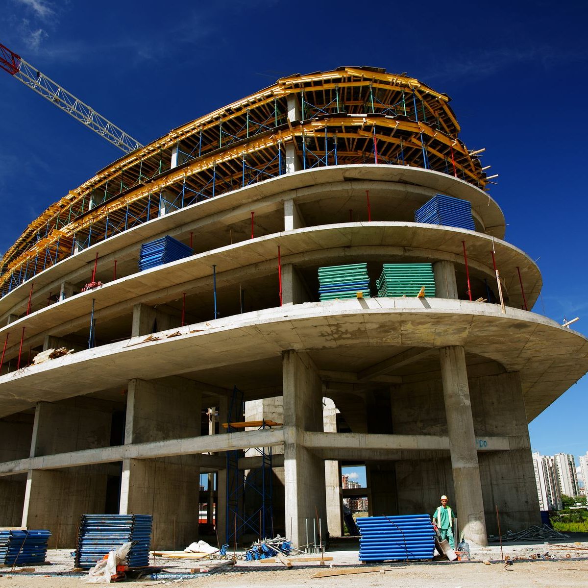 Rohbau eines Gebäudes mit gekrümmter Fassade und Baukran vor blauem Himmel